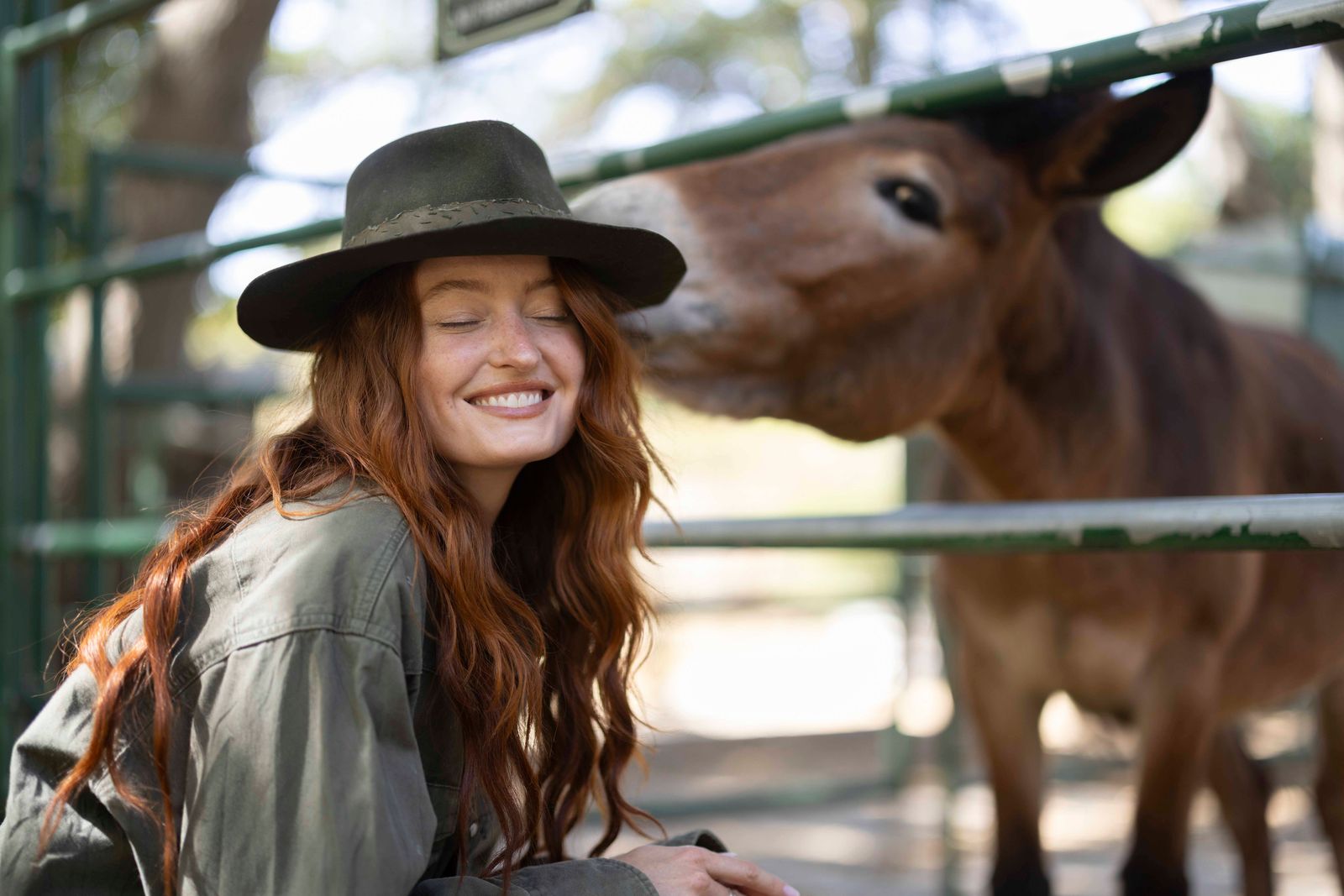 Model in an olive shirt and hat, smiling beside a mule